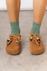 Zueco de cuero gamuzado color beige, con cordones decorativos con cuentas y piezas envueltas en cuero. Tiene plantilla acolchada y base liviana.