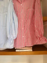 Camisa de organza a rayas verticales rojas y blancas, con mangas largas abullonadas y puños elásticos.