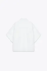 Camisa azul de cuello solapa y manga corta con dobladillo. Tiene dos bolsillos de parche en el pecho, bajo asimétrico con aberturas laterales y cierre frontal con botones ocultos.