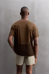 Camiseta deportiva marrón confeccionada en tejido técnico ligero y elástico con estructura perforada. Cuello redondo, manga corta y bajo asimétrico con aberturas laterales. Detalle de logo estampado.