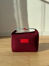 Neceser color beige de forma rectangular, con cierre superior y asa de mano.