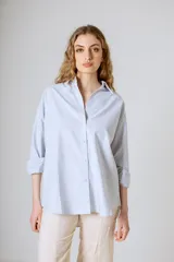 Camisa celeste de corte clásico, con cuello camisero, mangas largas con puños abotonados y cierre frontal con botones.