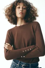 Sweater negro de punto liso con cuello redondo y mangas largas con botones dorados en los puños.