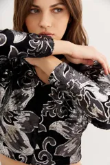 Blazer negro de terciopelo con estampado floral plateado, corte cropped y mangas largas.