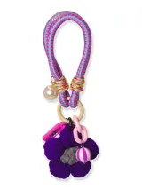 Llavero con cordón elástico celeste y rosa, adornado con una cuenta perlada, una flor tejida violeta con centro gris, una cuenta rayada blanca y violeta, un dije rosa con forma de pastilla y eslabones de cadena rosa.