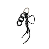 Llavero con cadena de eslabones plateados y charms colgantes: cadena de eslabones gruesos negros, cordón trenzado negro y blanco, y dije de corazón plateado.