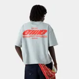 Camiseta de corte holgado (boxy fit) color verde claro con estampado grande en la espalda en color rojo que incluye el logo 'eme' y el texto 'building a community through gratitude'.