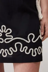 Minifalda negra de tiro alto con bordado blanco en el ruedo y cinturón de soga.