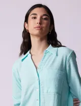 Camisa celeste texturada con cuello con solapa y abertura central con botones. Delantera con bolsillo aplicado y largo de manga regulable con presilla y botón.