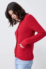Chaqueta tejida roja con botones metálicos dorados y cuello redondo.