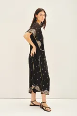 Vestido largo negro de gasa traslúcida bordada con canutillos, lentejuelas y mostacillas. Tiene escote en V, mangas amplias de largo irregular, gancho oculto en el escote y viso al tono con breteles regulables y puntilla en el escote.