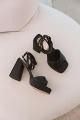 Sandalias negras de cuero sintético con plataforma y tacón bloque. Tiras finas cruzadas en el empeine y tobillo con hebilla dorada.