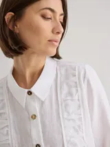 Camisa negra de lino con corte femenino, cuello clásico, cierre frontal con botones y mangas 3/4 con puños enrollados. Presenta detalles de frunces verticales en el frente y bolsillos de parche a la altura de la cadera.