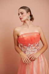 Vestido largo de fiesta, strapless, con busto drapeado y falda de tul con degradé de color coral a blanco. Presenta bordados florales en el corpiño.