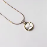 Collar con dije circular de nácar, en combinación de plata y oro, de 45 cm de largo.