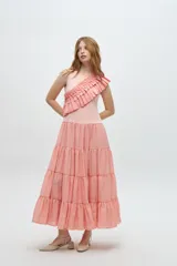 Vestido largo color salmón, con cuerpo ajustado de algodón y falda amplia de rayon, nylon, poliéster y elastano. Presenta un volante plisado en diagonal desde el hombro hasta la cintura.