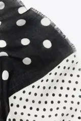 Pañuelo cuadrado con estampado de lunares blancos sobre fondo negro en la mitad superior y lunares negros sobre fondo gris en la mitad inferior.