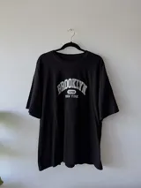 Remera negra de corte amplio con estampa frontal que dice "Brooklyn 1898 New York" en color blanco.