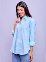 Camisa blanca de algodón, corte holgado, con cuello clásico y botones frontales. Las mangas son largas y se ven remangadas.