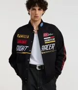 Campera negra con cuello alto, cierre de botones y estampado estilo racing con logos y textos en amarillo, rojo y blanco. Tiene bolsillos laterales y mangas largas con detalles estampados. Marca Blue Steel.