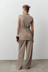 Pantalón de sarga color beige, de tiro medio con cintura elástica en la espalda, bolsillos laterales de plastrón con botón metálico y pierna ancha.