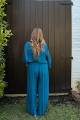 Enterito de mujer color azul piedra, con escote en V, mangas tipo capa y cintura fruncida elástica. El pantalón es de pierna ancha y fluida.