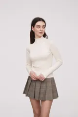 Polera de tejido canalé de color crudo, con cuello alto y mangas largas.