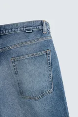 Bermuda de denim de algodón, color gris claro lavado, de corte ancho (baggy fit) y largo hasta la rodilla. Presenta cinco bolsillos y cierre frontal con cremallera y botón.