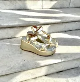 Sandalias de plataforma doradas, con suela ancha y tiras anchas cruzadas en el empeine y una tira ajustable en el tobillo.