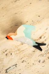 Broche con forma de colibrí con cuerpo blanco, cabeza naranja, pico negro, ala celeste y cola negra.
