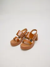 Sandalias de cuero color crema con plataforma, taco cuadrado y tiras anchas con argollas metálicas.