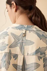 Vestido camisero corto de lino color blanco con estampado de estrellas de mar y algas en azul. Tiene cuello mao, mangas largas y cierre frontal con botones.