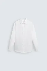 Camisa blanca de manga larga con cuello italiano y puños abotonados. Presenta un tejido con estructura y corte regular fit.