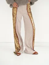 Pantalón de brocato color champagne con lentejuelas doradas en los laterales, tiro medio, cuatro bolsillos, cierre frontal con botón de guampa y bajo acampanado con tajos laterales.