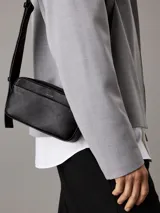 Bolso bandolera negro de Calvin Klein, confeccionado en piel sintética suave. Tiene correa ancha ajustable, cierre de cremallera, bolsillo exterior y bolsillo interior.
