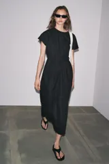 Vestido midi color marrón confeccionado en hilatura con mezcla de algodón y lino. Tiene cuello redondo, manga corta caída y detalle de pliegues en la cintura. Cierre en la espalda con abertura y botón.