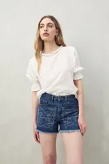 Short de jean azul con bordado floral en el frente y ruedo desflecado.