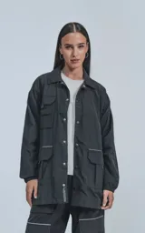 Campera negra oversize con broches en el delantero, forro de red, múltiples bolsillos con detalles reflectivos y puños elásticos.