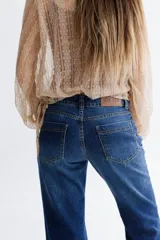 Pantalón de jean azul gastado con proceso de gastado localizado, corte con cintura media entallada y piernas de corte recto (Boot Cut) levemente oxford desde la rodilla.