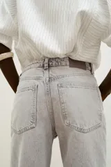 Jeans de tiro alto color negro lavado, con cintura cruzada, cinco bolsillos y pernera recta. El bajo está acabado en vuelta y tiene cierre frontal cruzado con cremallera y botones.