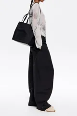 Bolso tote pequeño marca Bimba y Lola, modelo Chihuahua, color marrón. Confeccionado en nylon con estructura blanda, doble asa de mano y asa de tejido, piezas de piel, cierre con botón de presión, logo grabado, acabados metálicos, bolsillo interior e interior con placa metálica logotipada.