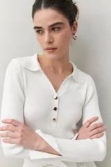 Sweater blanco de punto acanalado con cuello tipo polo y botonadura frontal de botones metálicos. Mangas largas con terminación en pequeñas aberturas.