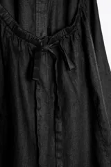 Vestido midi negro de lino, con cuello halter, hombros descubiertos, espalda descubierta, cierre frontal con botones y bajo asimétrico.