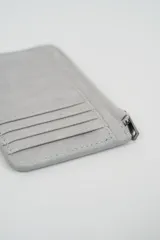 Billetera pequeña color gris claro con cierre de cremallera perimetral y tachas metálicas oscuras distribuidas en el frente.