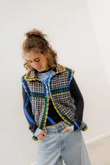 Chaleco negro de corderito con cierre de alamares, tejido a mano en crochet con detalles en amarillo, verde y azul. Cuello alto con interior a cuadros. Talle oversized.