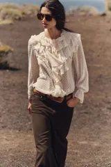 Blusa color crema semitransparente con cuello redondo con volantes y cordón. Manga larga acabada en elástico y volante. Cierre frontal con botones.