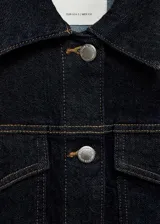 Chaqueta de jean azul oscuro con cuello camisero, cierre frontal abotonado, mangas largas con puños abotonados, dos bolsillos con solapa en el pecho y costuras decorativas. Confeccionada en tejido de algodón.