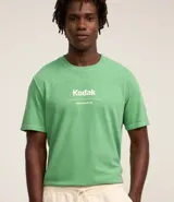 Remera verde con estampa de la marca Kodak y photoprint de playa paradisíaca.