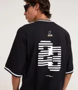 Remera deportiva de algodón, color negro, con corte oversized, cuello redondo y mangas cortas. Presenta ribetes contrastantes en blanco en el cuello y los bordes de las mangas. Tiene un estampado localizado en el pecho con tipografía en relieve y un pequeño logo en el lateral superior.
