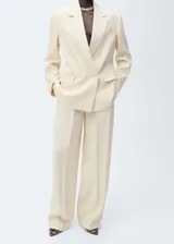 Conjunto color crema compuesto por un blazer de doble botonadura con solapas de muesca y bolsillos de parche, y un pantalón de corte wide leg con pinzas y cierre oculto.